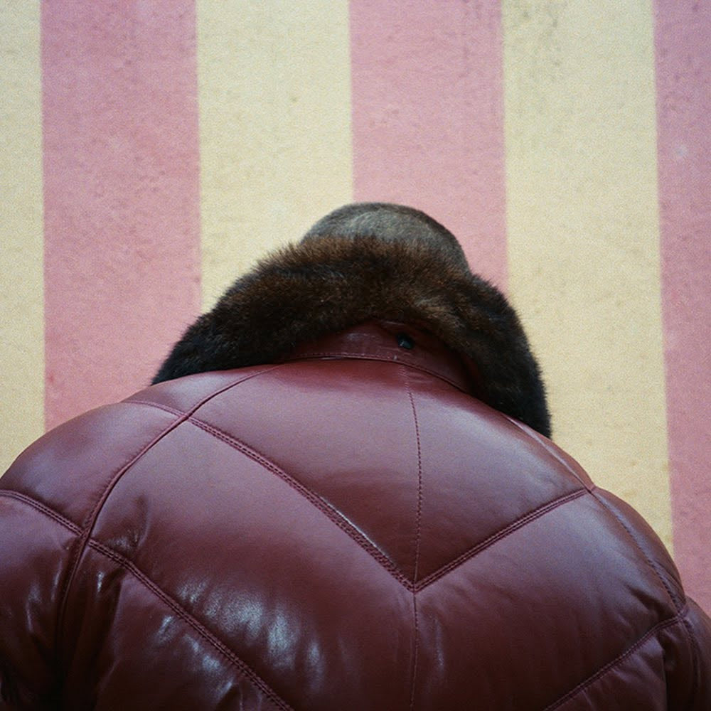 Man wearing Double Goose burgundy leather bomber jacket with fur collar against striped wall