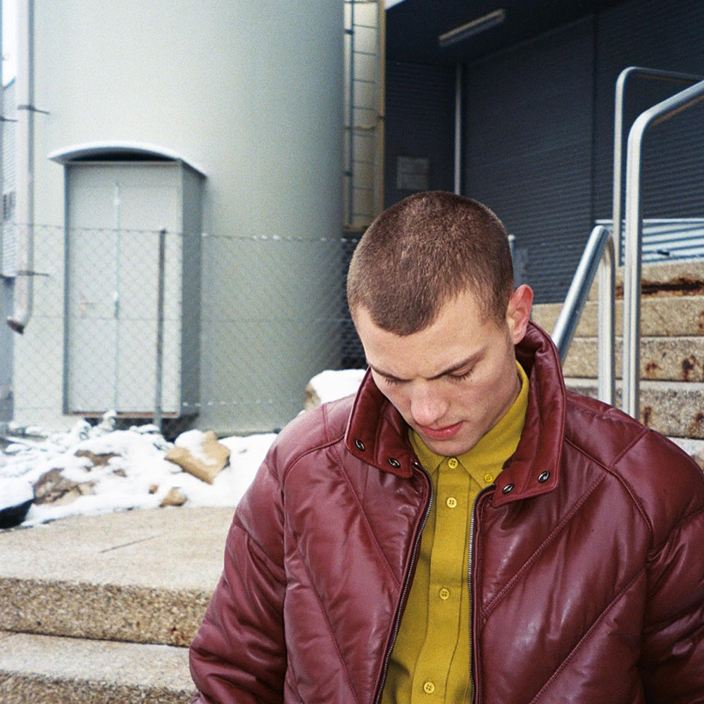 Man wearing Double Goose burgundy leather V-Bomber jacket, street style seated portrait