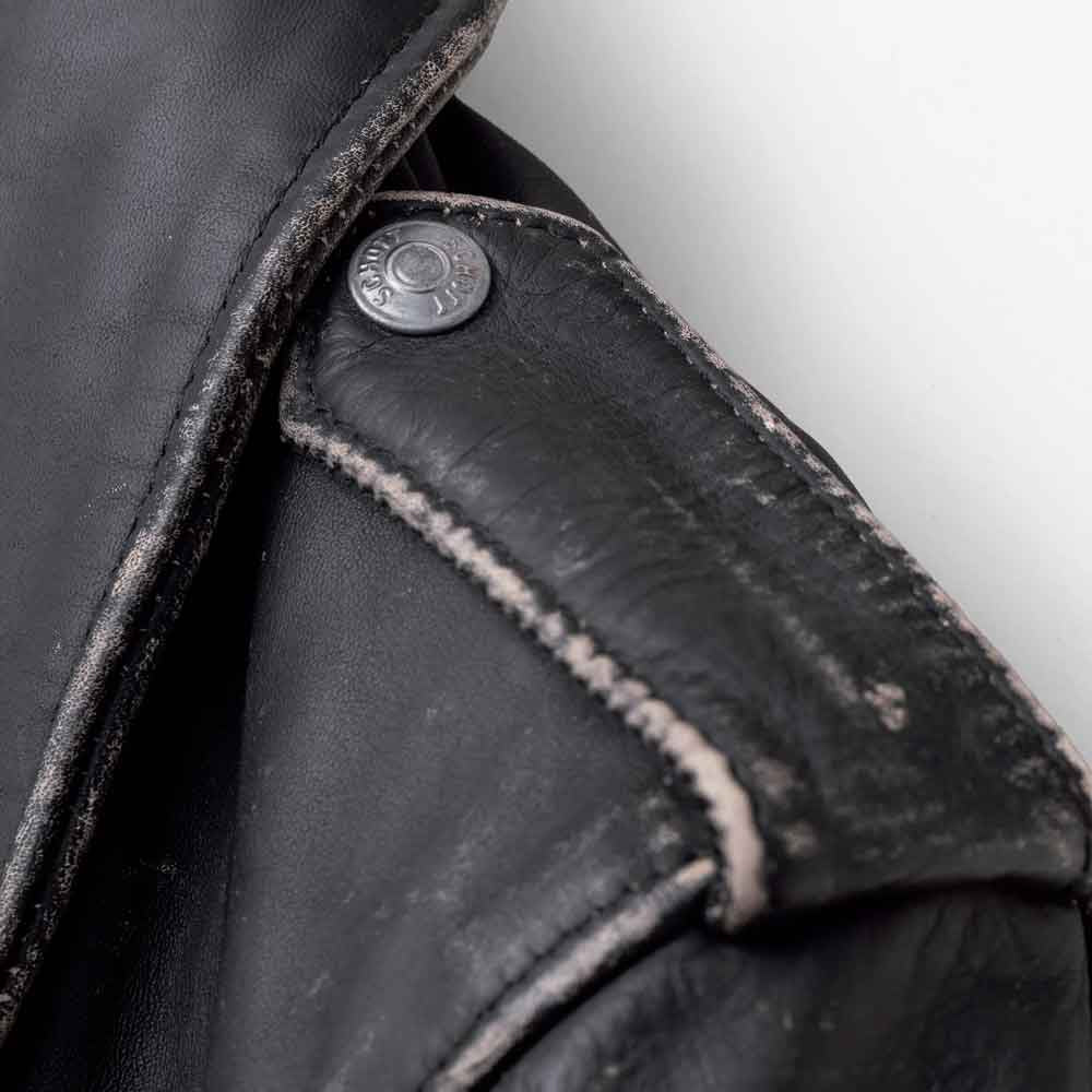 Detailed view of worn black leather shoulder epaulette, silver snap and raised lapel edge on men’s double-rider jacket