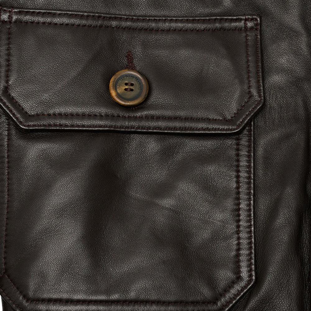 Close view of espresso lambskin grain, tonal topstitching, horn button and geometric flap patch pocket on A-1 bomber.