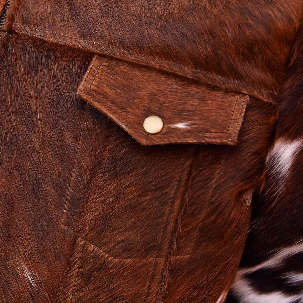 Detailed view of a pointed chest pocket flap with antique-brass-tone snap on brown hair-on cowhide