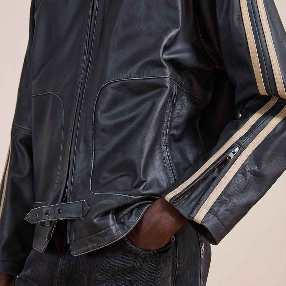 Detail of curved zip pocket, double racing bands, zippered cuff and adjustable leather waist tab on men’s black racer jacket