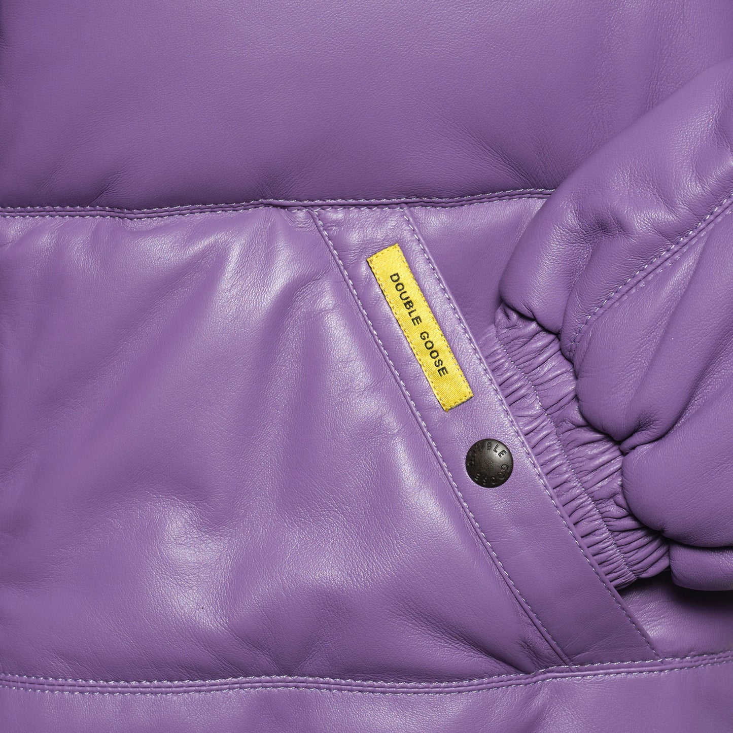 Close-up details of a welt-angled hand-warmer pocket with a branded snap-button on lilac leather.