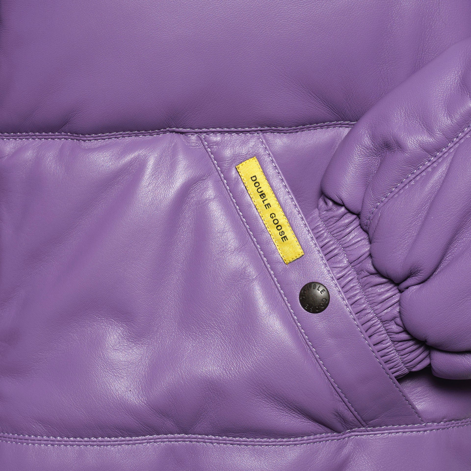 Close-up details of a welt-angled hand-warmer pocket with a branded snap-button on lilac leather.