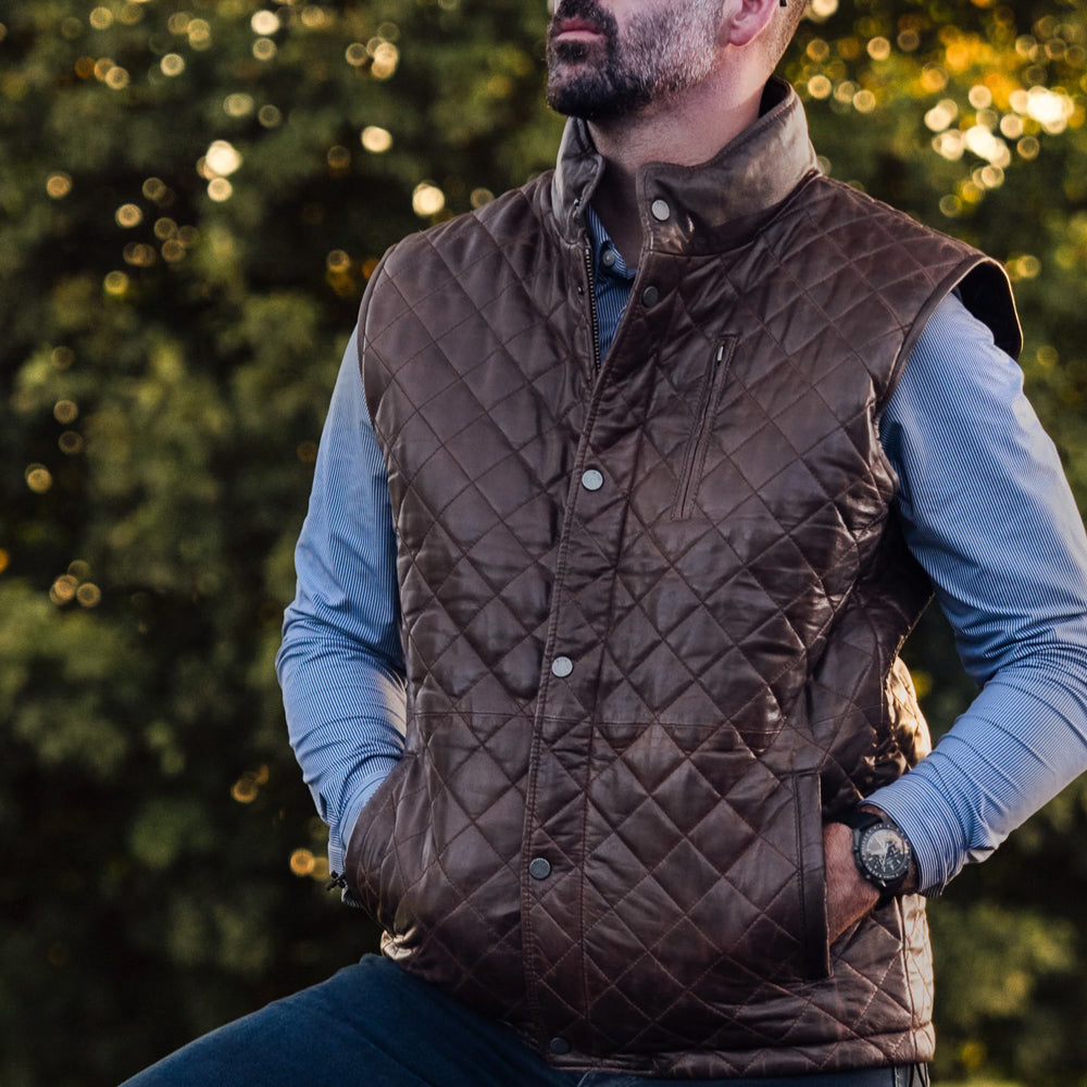Lifestyle shot of a man in the brown moto vest with both hands resting in the zippered slant pockets.