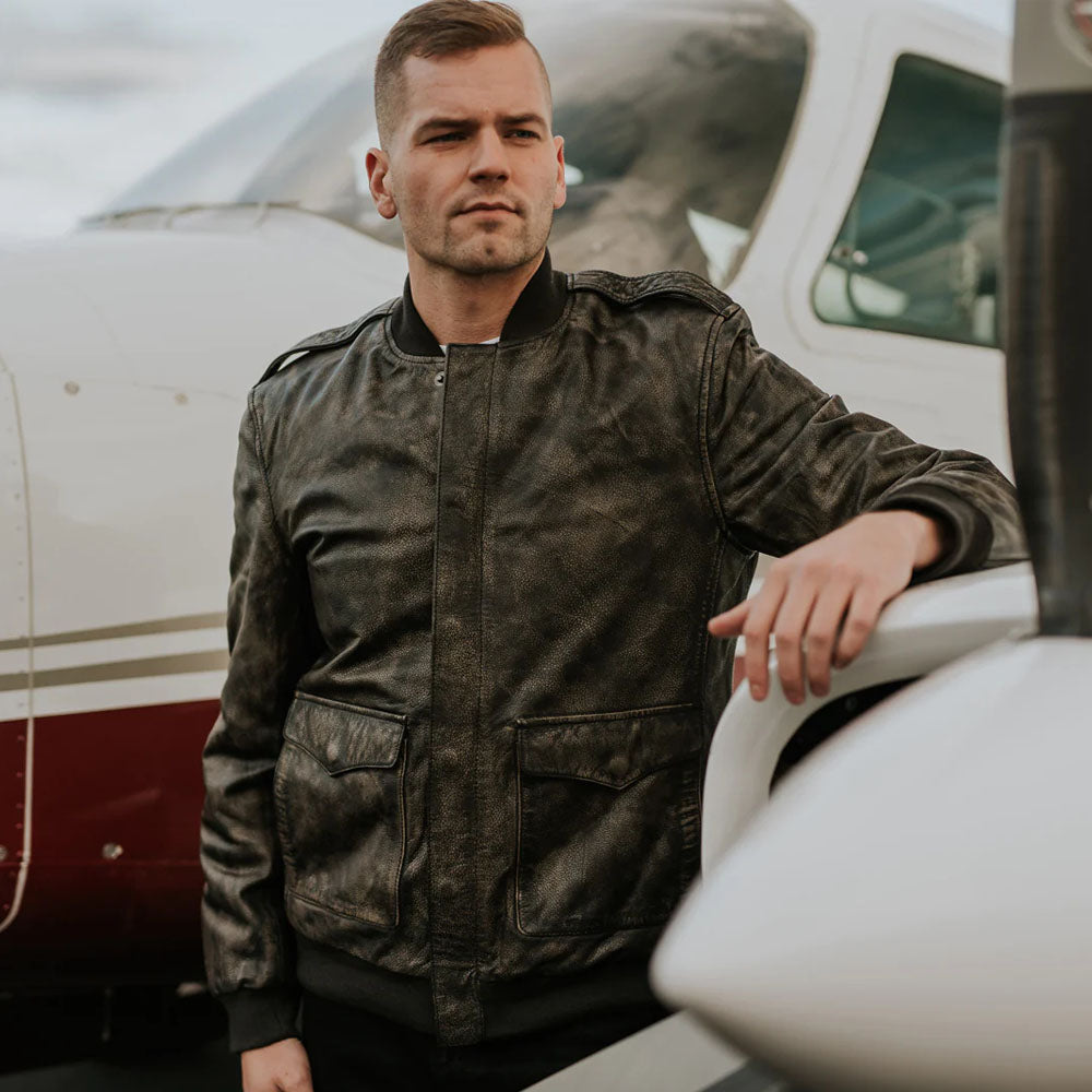 Man wearing distressed brown leather bomber jacket outdoors near an aircraft