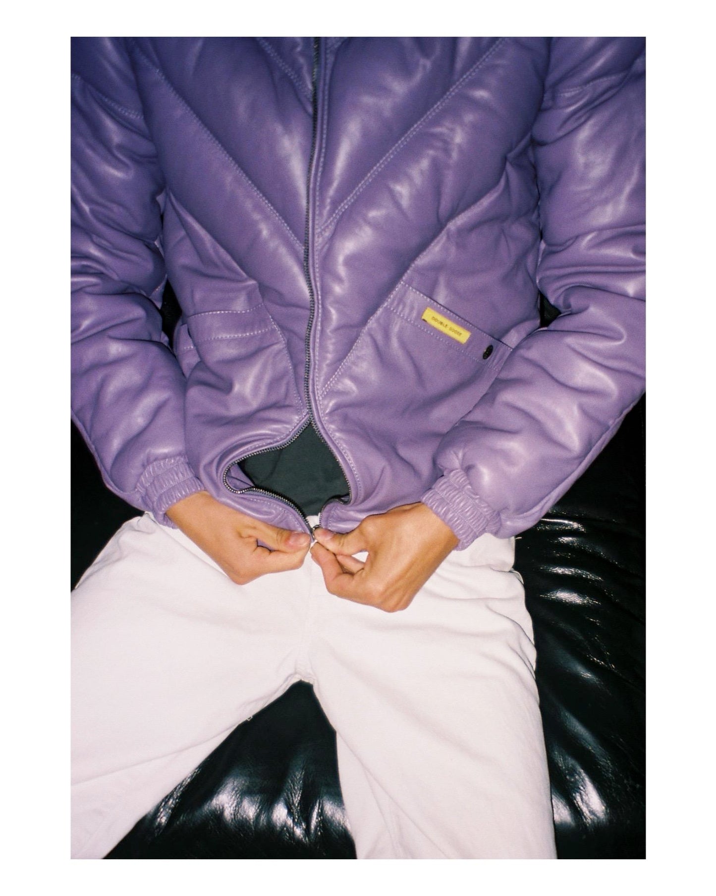 High-intent lifestyle shot of a man wearing the lilac leather jacket while closing the front metal zipper.
