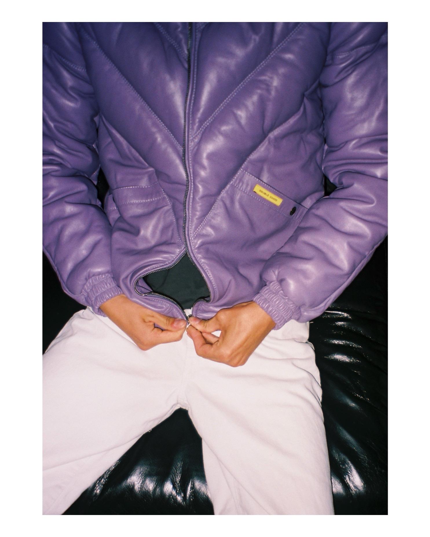 High-intent lifestyle shot of a man wearing the lilac leather jacket while closing the front metal zipper.