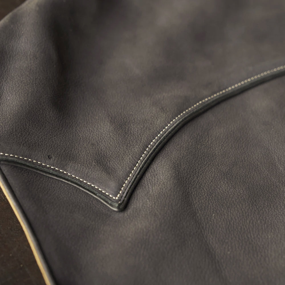 Close-up of matte charcoal top-grain nubuck texture beside the raised black leather yoke border