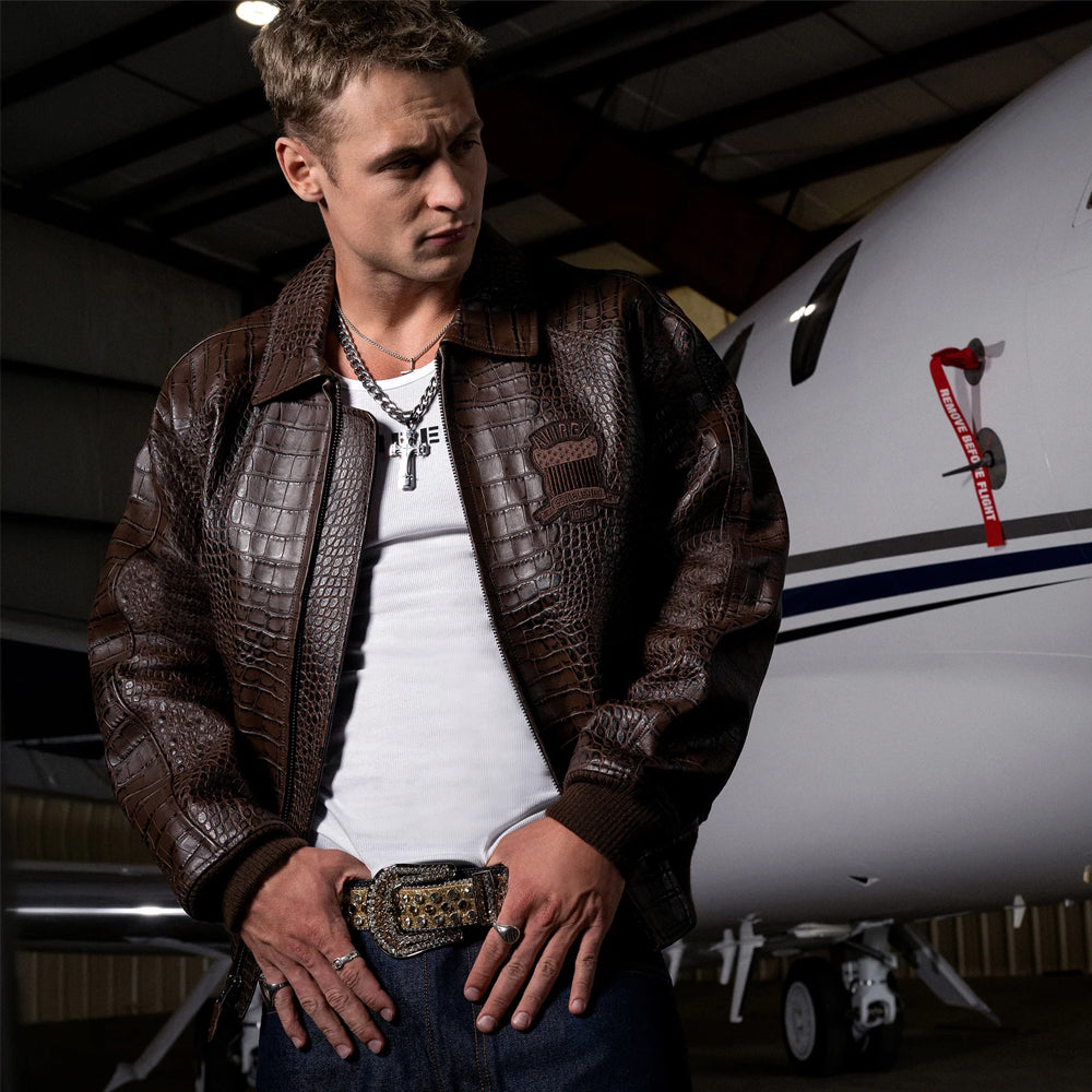 Man wearing the brown Avirex embossed leather bomber over a white top beside an aircraft