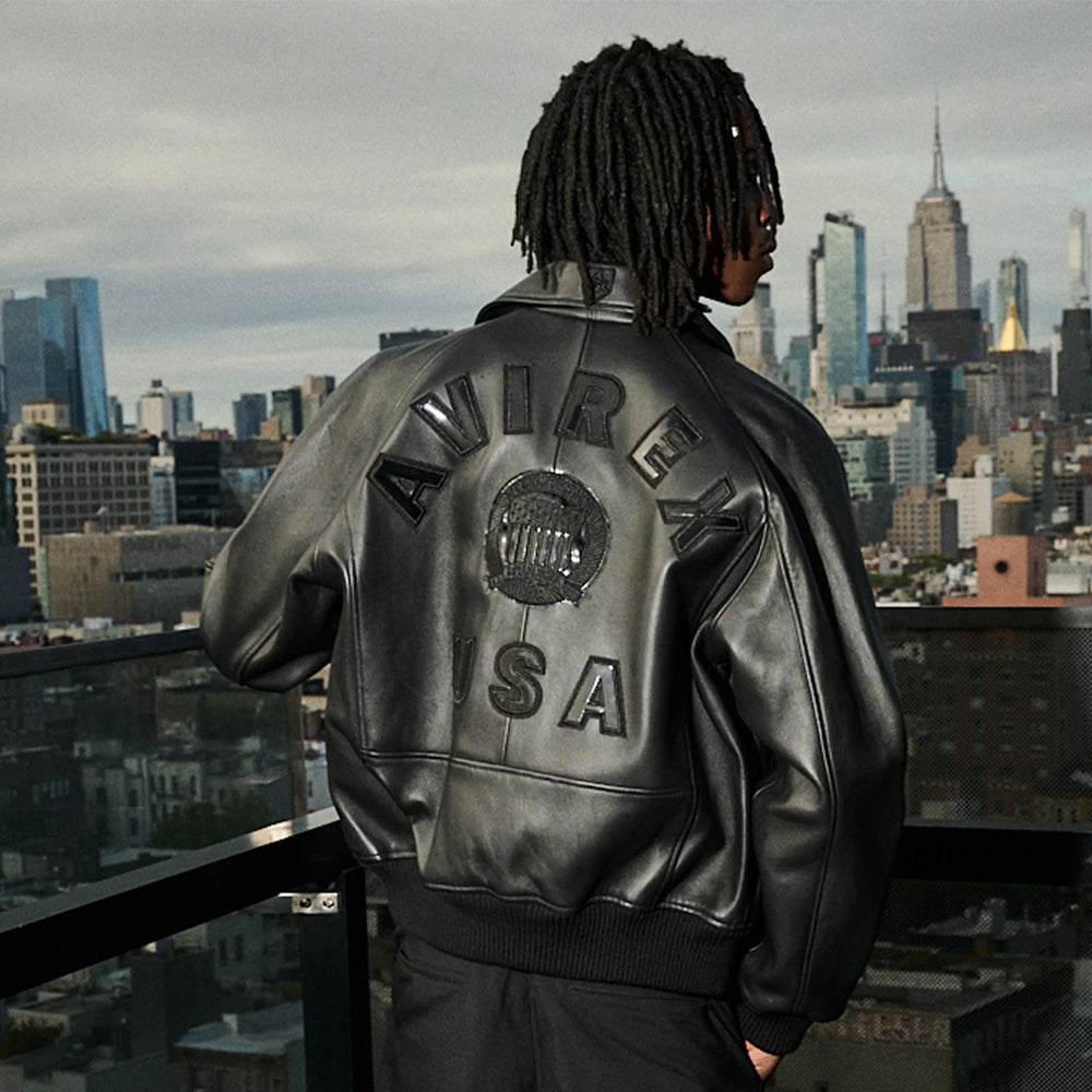 City rooftop back angle of men’s Avirex Iconic lamb leather bomber with glossy circular crest and black USA appliqué