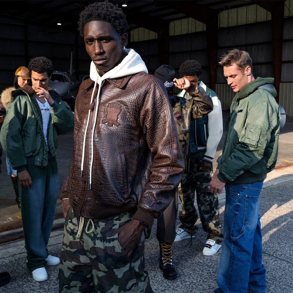 Brown Avirex textured leather bomber layered over a white hoodie with camouflage cargo pants
