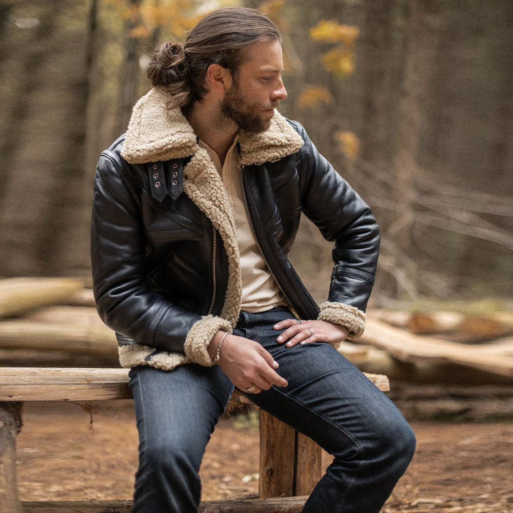 Model sitting outdoors wearing men's black chevron B-3 aviator shearling flight jacket paired with jeans