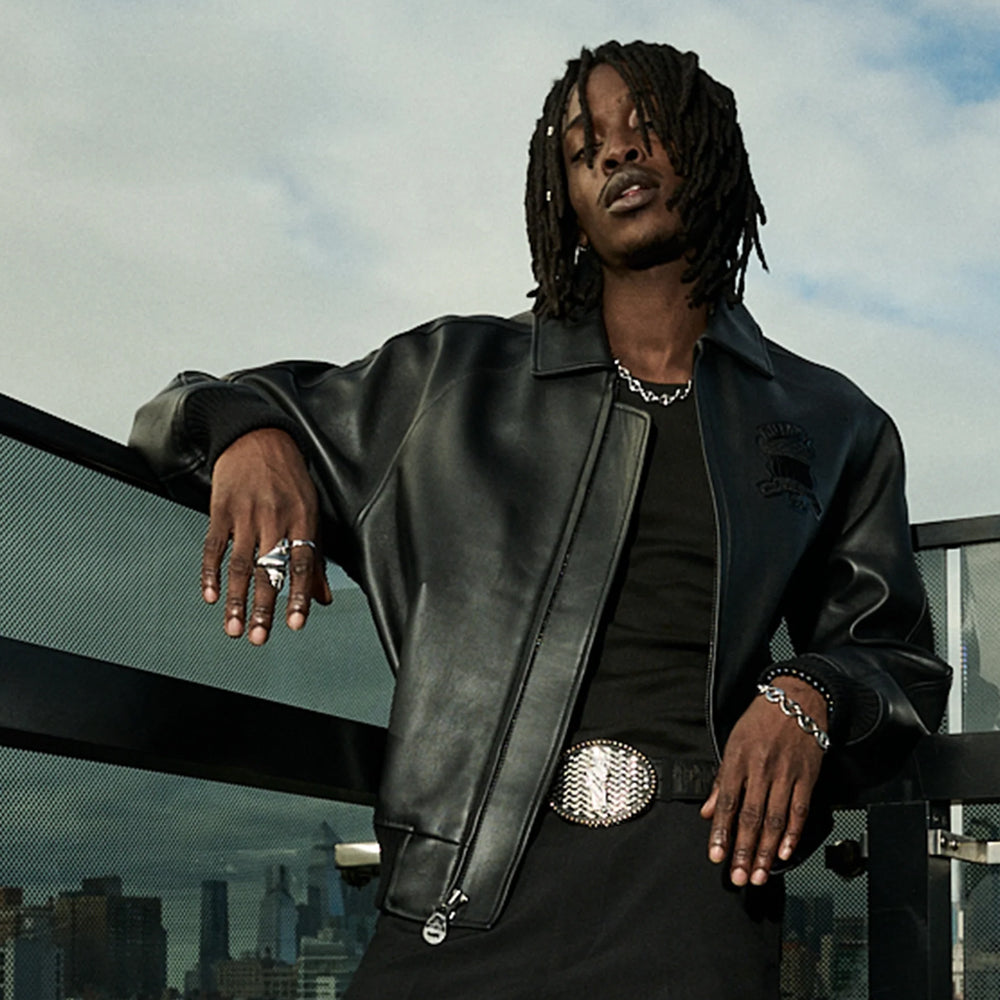 Urban campaign view of men’s black Avirex Icon jacket worn open over a black top with tonal embroidered chest crest