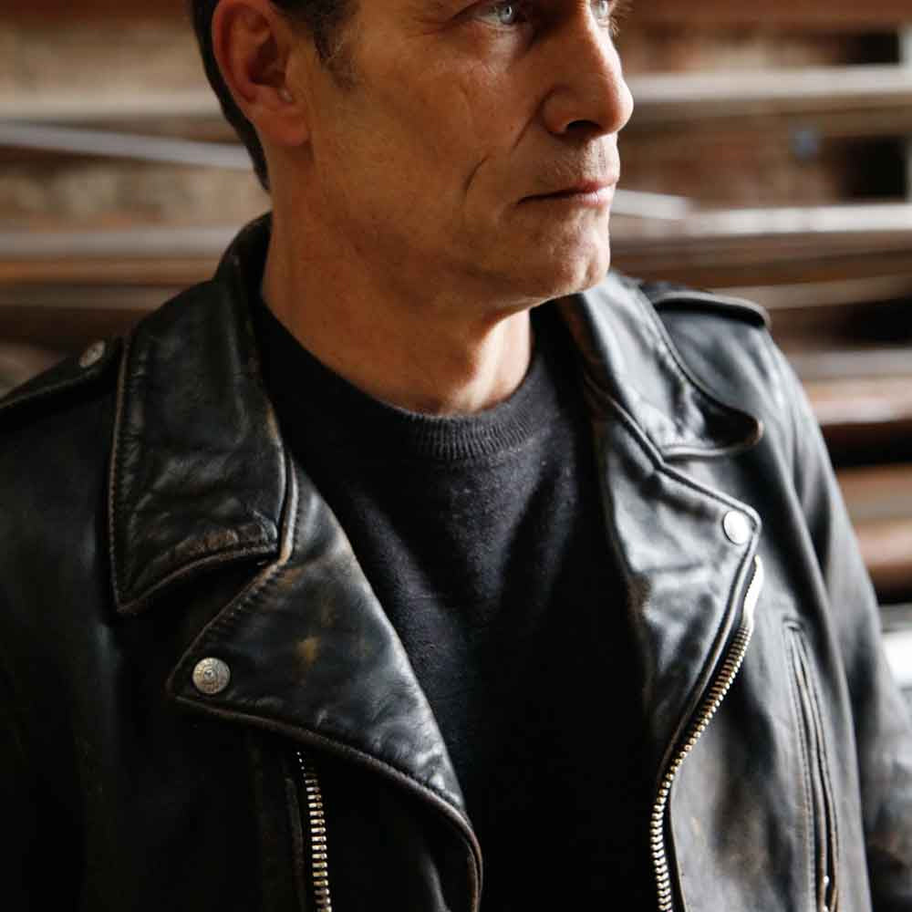 Model wearing men’s distressed black cross-zip leather jacket with broad snap lapels and silver zipper hardware