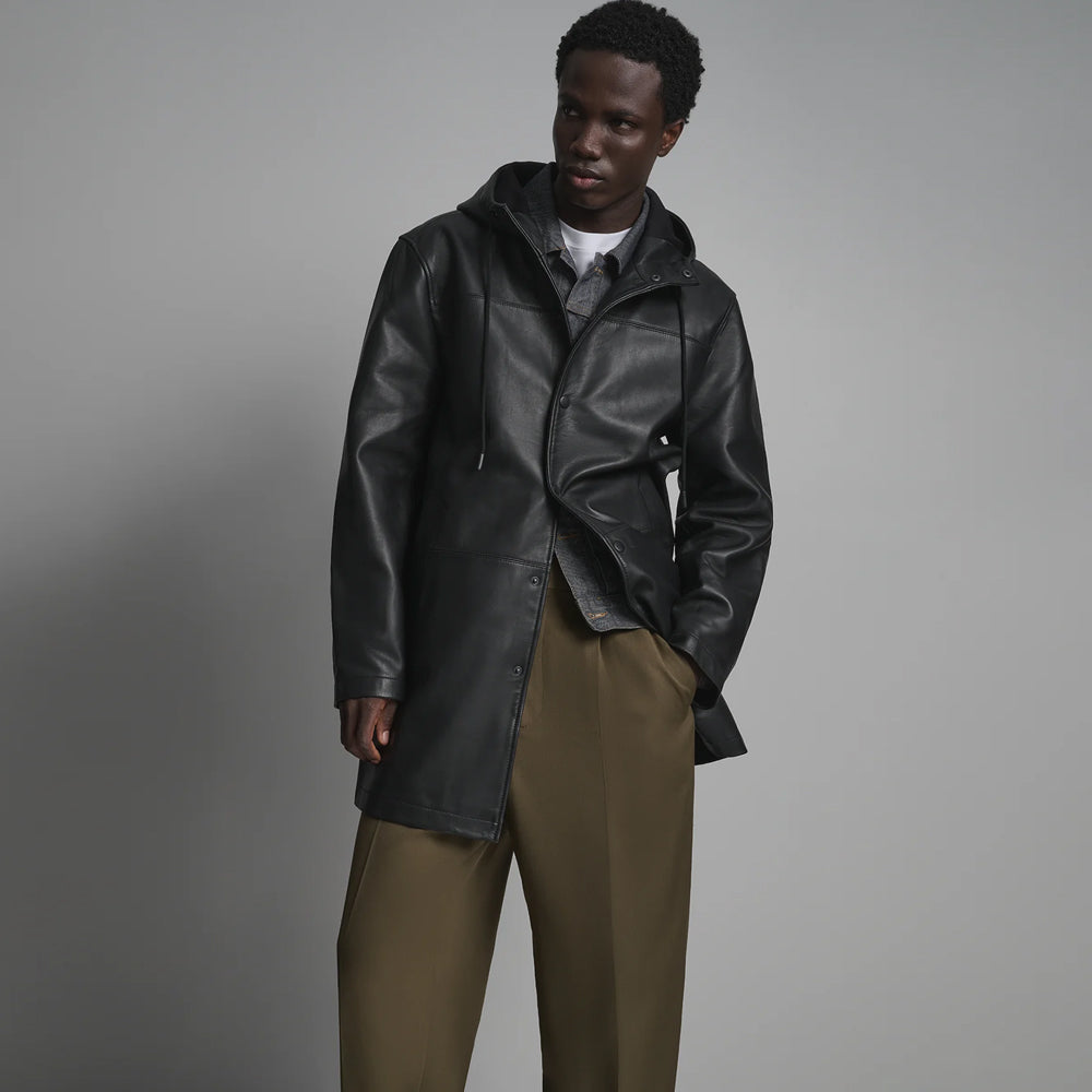 Three-quarter view of men’s black longline leather hoodie with attached drawstring hood, tonal snap front and medium-thigh hem.