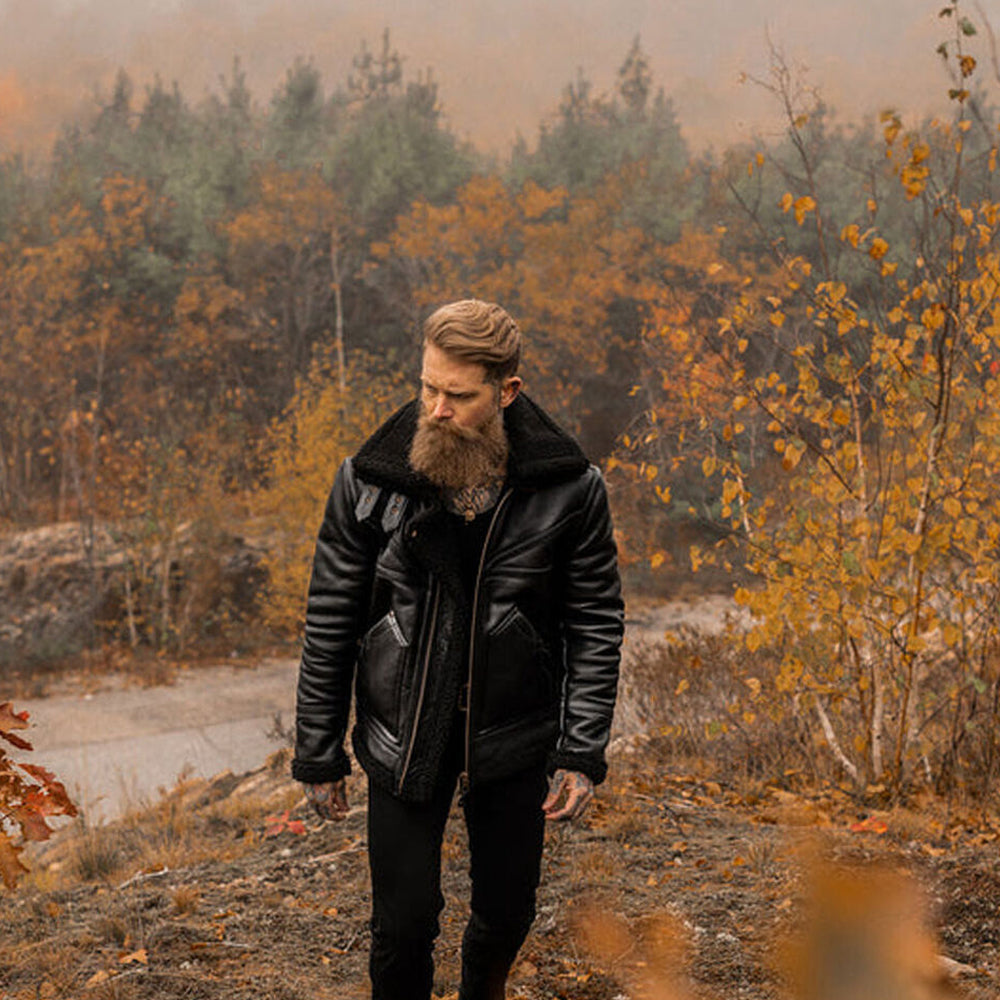 Full body view of bearded model wearing black shearling aviator jacket walking through autumn woods