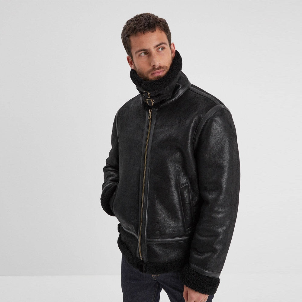 Model wearing men’s black shearling aviator jacket with raised double-buckle collar, antique zipper, and side waist adjuster