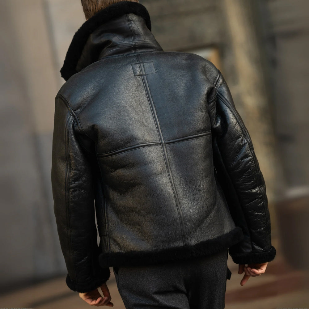 Back view of men’s black sheepskin jacket showing center seam, curved shoulder yoke and shearling-trimmed hem