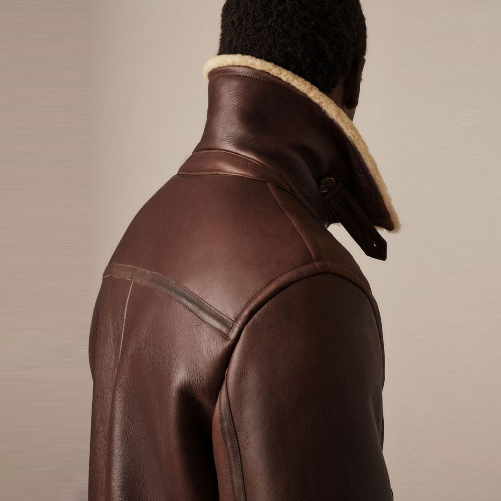 Back view of men's brown shearling flight jacket showing high stand collar with buttoned throat latch strap