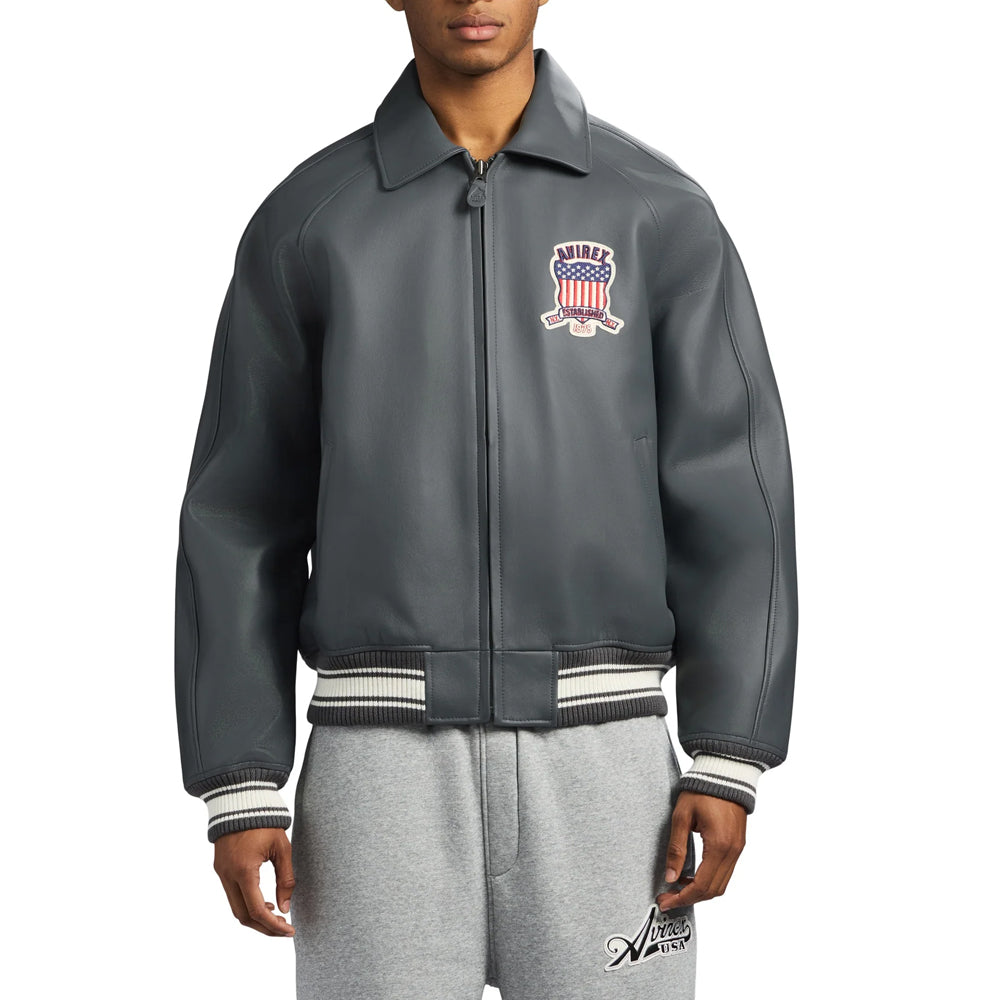 Model wearing men’s charcoal gray Avirex Icon bomber with center zipper, welt pockets and striped knit waistband