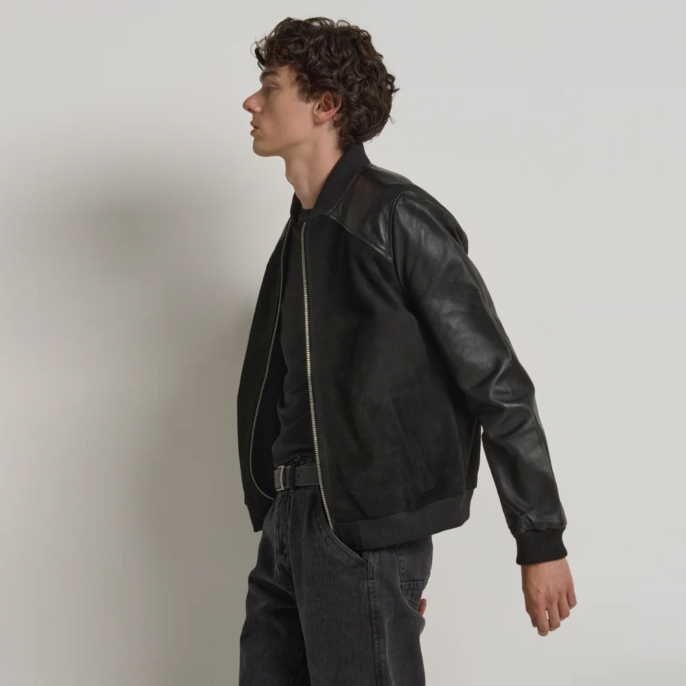 Side profile of men’s mixed-texture bomber showing matte suede torso, smooth leather sleeve and angled welt pocket