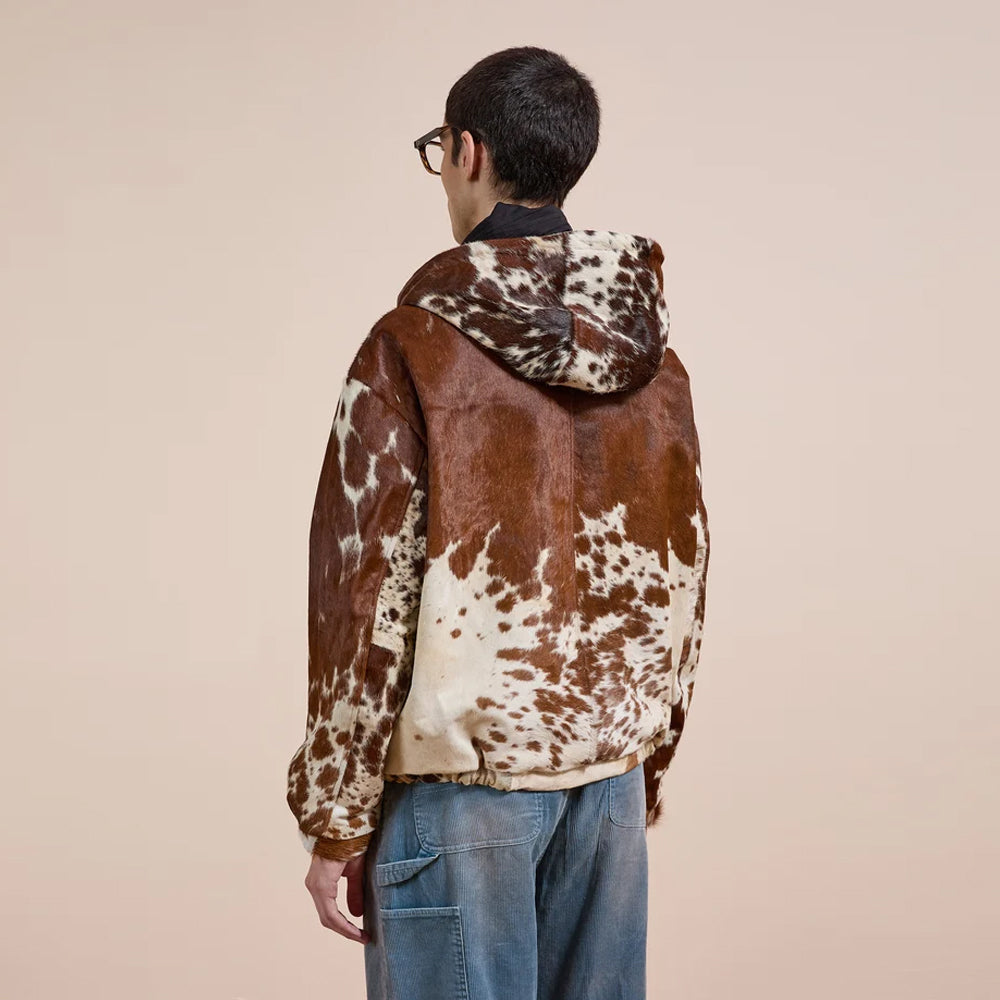 Back three-quarter view of the cowhide hoodie jacket showing its broad natural hide panel, shaped hood and elastic hem