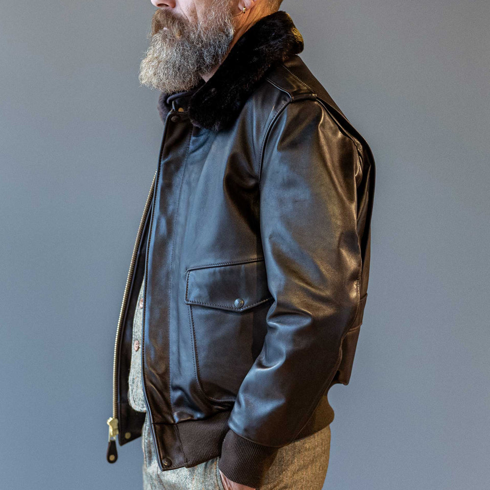Side profile view of men's dark brown military flight jacket displaying shoulder epaulettes and ribbed wrist cuff.