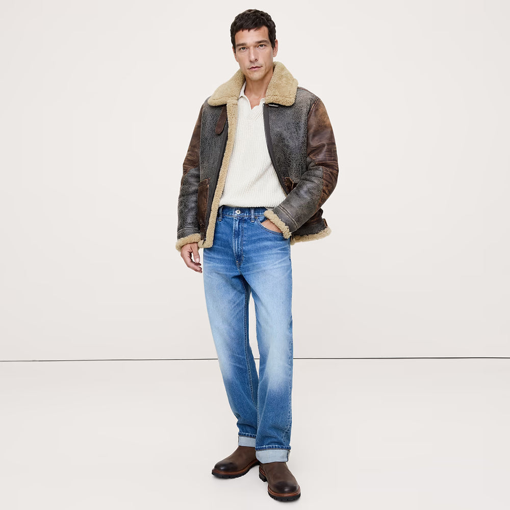 Full-body view of man wearing a distressed brown B-3 shearling aviator jacket with blue jeans