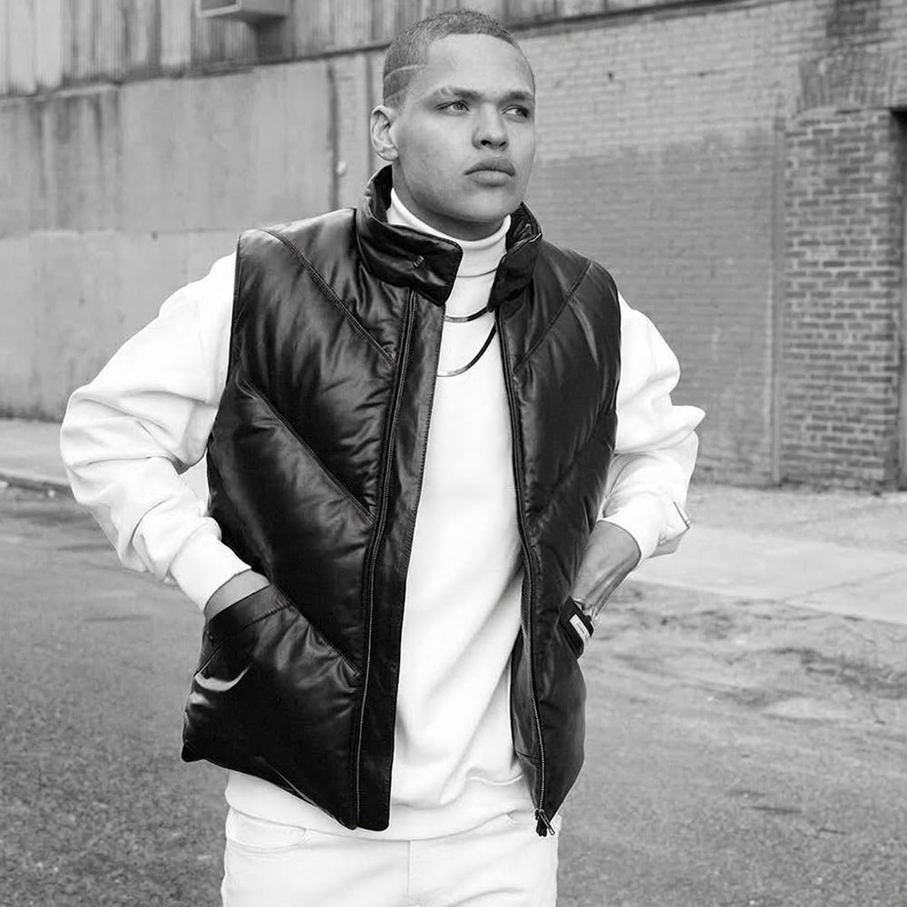 Male model wearing a black Double Goose leather down vest over a white sweatshirt in an urban setting