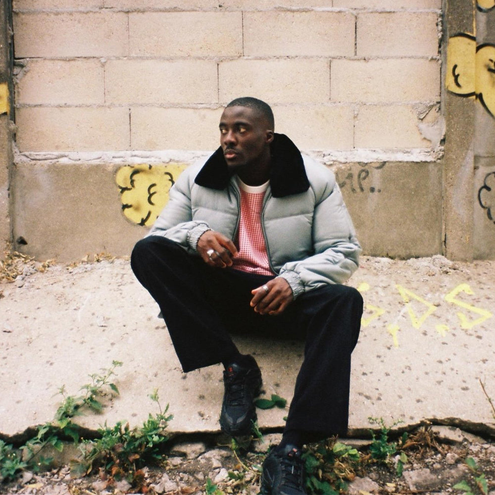 Man wearing the light grey Double Goose puffer bomber with black shearling collar in an urban street setting