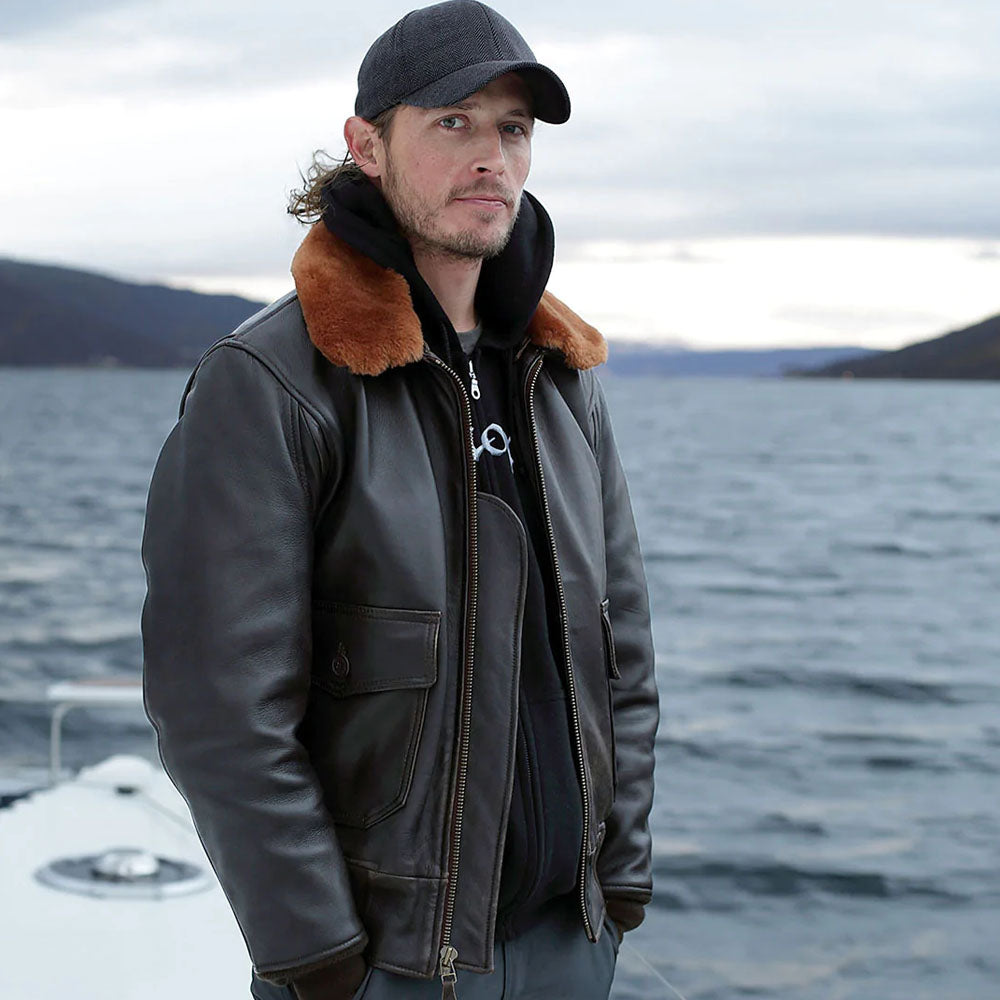 On-model view of men's espresso G-1 shearling bomber jacket worn unzipped over black hoodie near waterfront.
