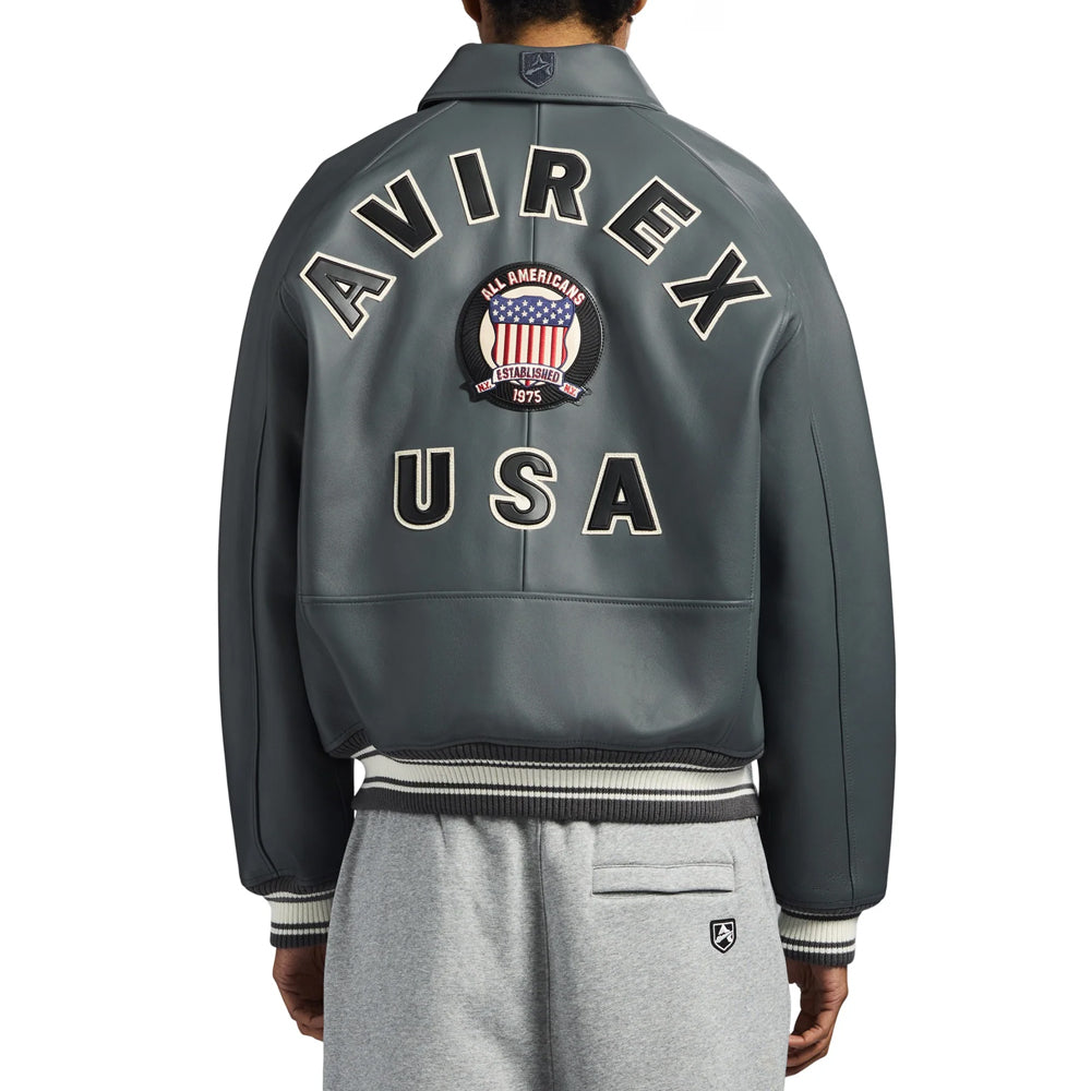 Rear model view of gray lamb leather bomber displaying cream-edged AVIREX lettering, USA patches and central crest
