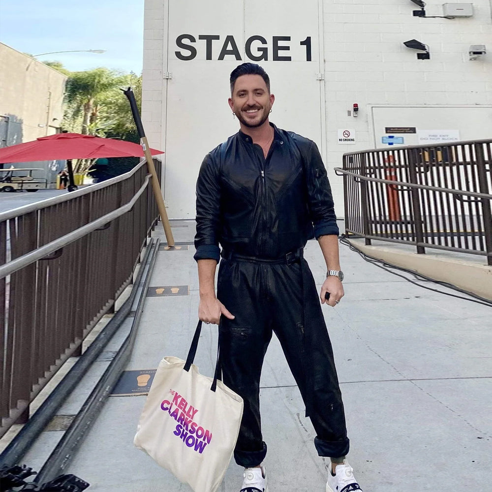 Model wearing men's black leather jumpsuit with front zipper, motocross collar and belted waist