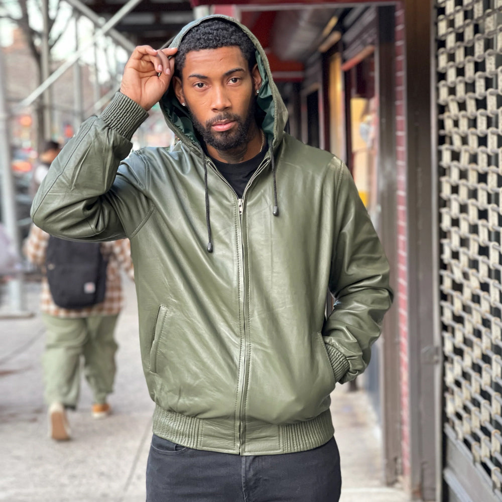 Front view of men’s olive green leather hoodie zipped closed with fixed hood raised, dark drawcords, welt pockets and ribbed trim.