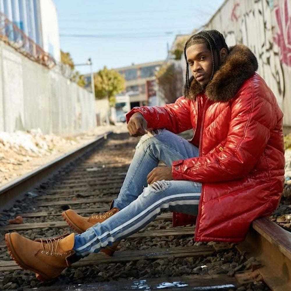 Man wearing red leather V-coat with fur collar seated on railroad tracks, streetwear lifestyle