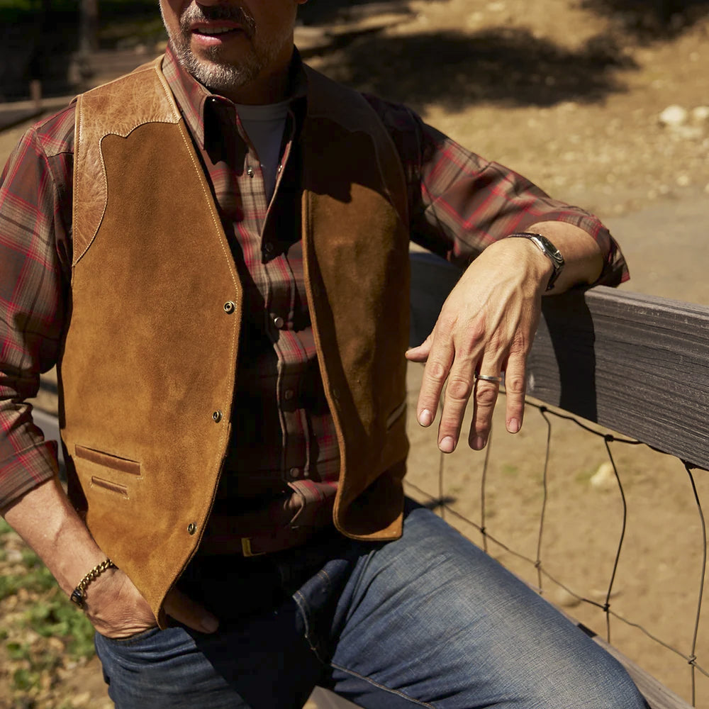 Man wearing a tan suede Western vest over a plaid flannel shirt with dark blue jeans at a ranch