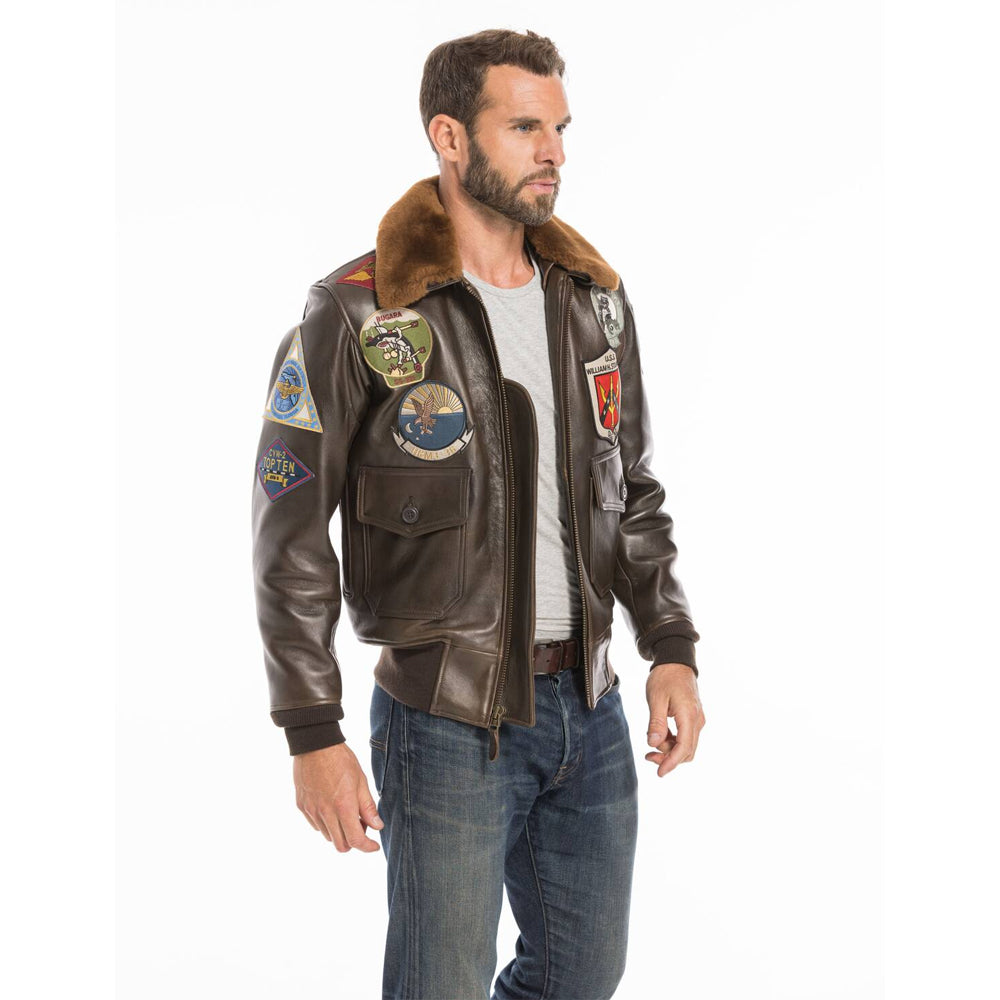 Three-quarter angled view of male model wearing men's Top Gun G-1 antique brown cowhide flight jacket featuring embroidered military patches and brown shearling collar.