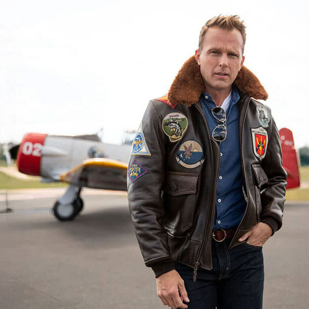 Model wearing men's Top Gun Maverick leather jacket standing in front of vintage aircraft.