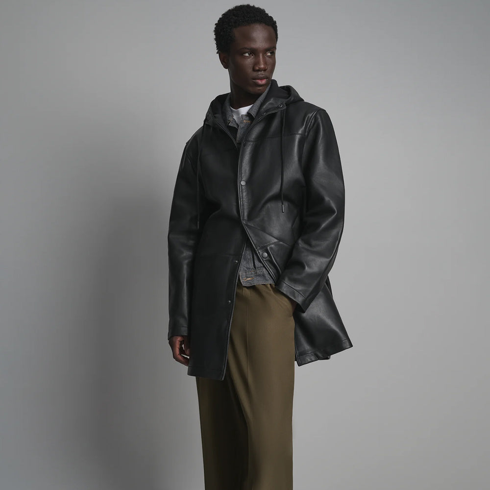 Angled view of men’s unlined black leather car coat with open snap placket, clean panel construction and straight hem.