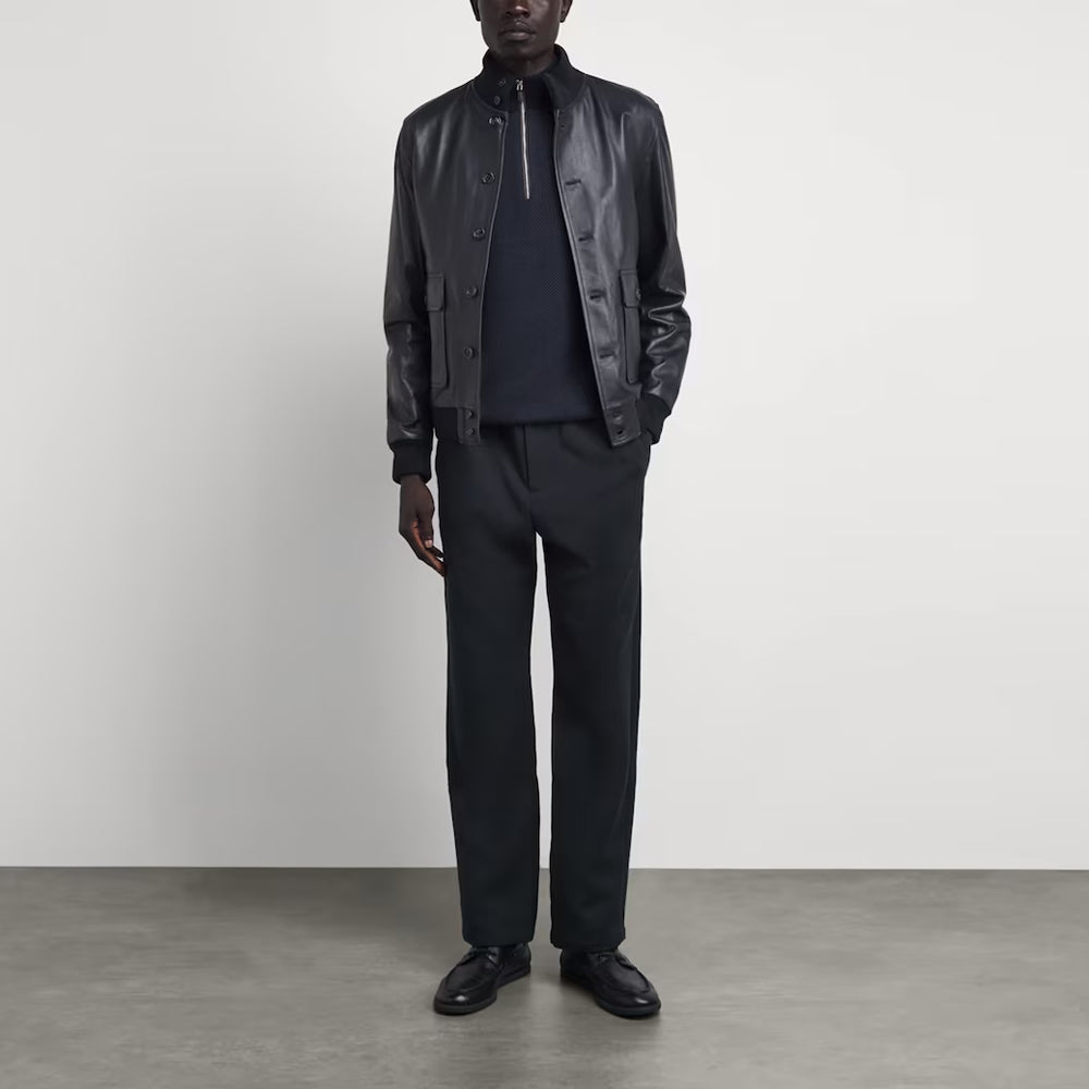 Full body view of model wearing men's Valstarino style black leather bomber jacket with tailored trousers.