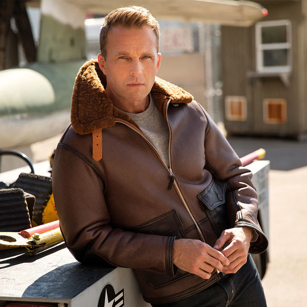 Model wearing men's vintage A-2 shearling aviator jacket outdoors in dark brown matte leather with contrast tan throat latch strap.