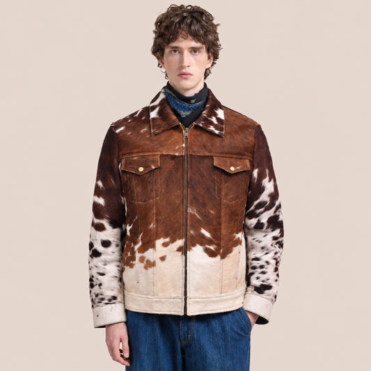 Model wearing a chestnut-brown and ivory hair-on cowhide trucker jacket with front zipper and snap-flap chest pockets