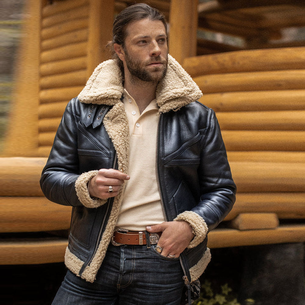 Male model wearing black chevron shearling B-3 aviator jacket with beige fleece collar standing outdoors