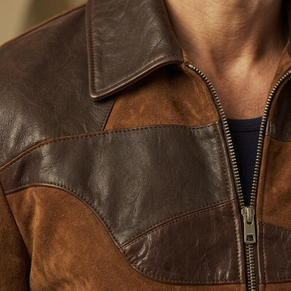 Close-up of men’s patchwork suede jacket with smooth chocolate leather collar, curved stitched yoke and metal zipper detail.