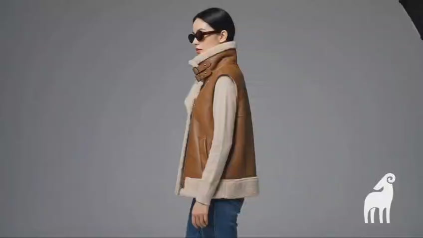 Women's tan sheepskin leather vest featuring a high oversized shearling collar, styled with blue jeans.