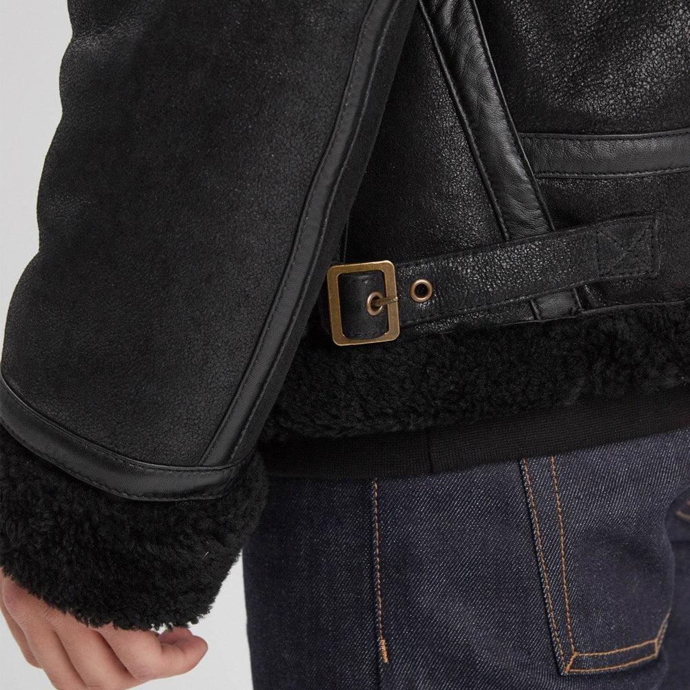 Antique-brass side buckle and eyelet adjuster on black RAF aviator jacket above the shearling-trimmed hem