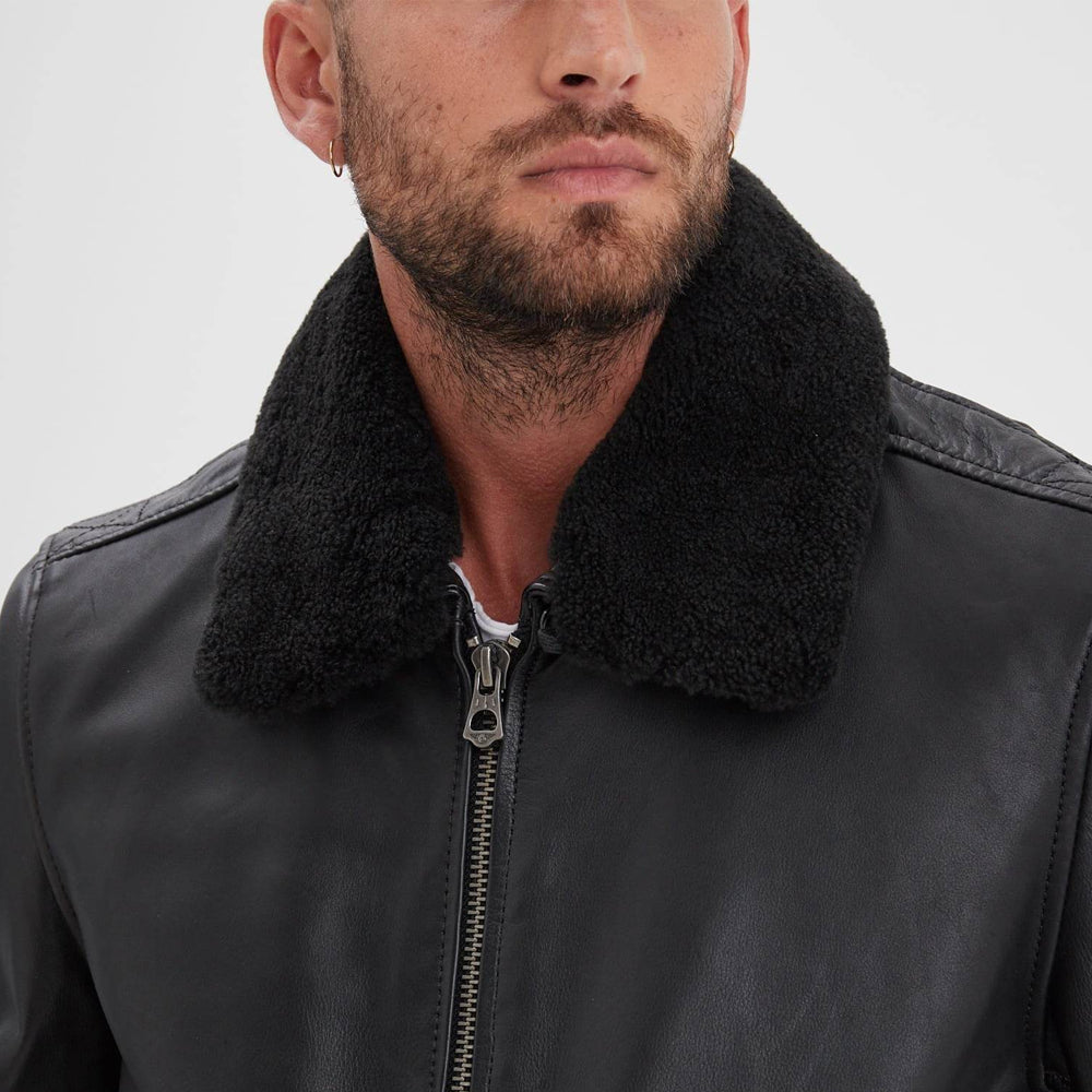 Close-up of removable black shearling aviator collar above the metal front zipper on a smooth black leather jacket.