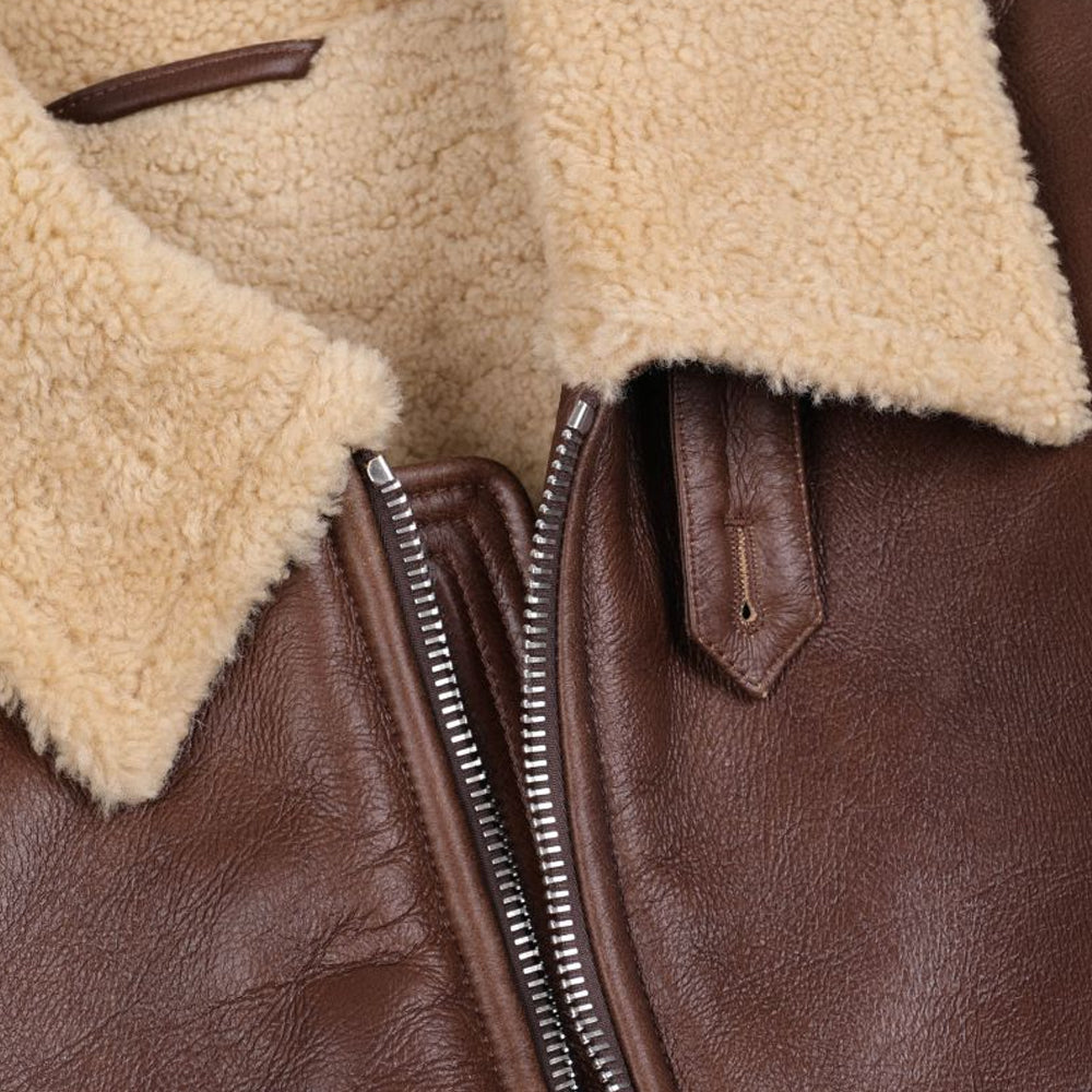 Close-up detail of cream shearling collar, silver heavy metal zipper, and leather button throat latch