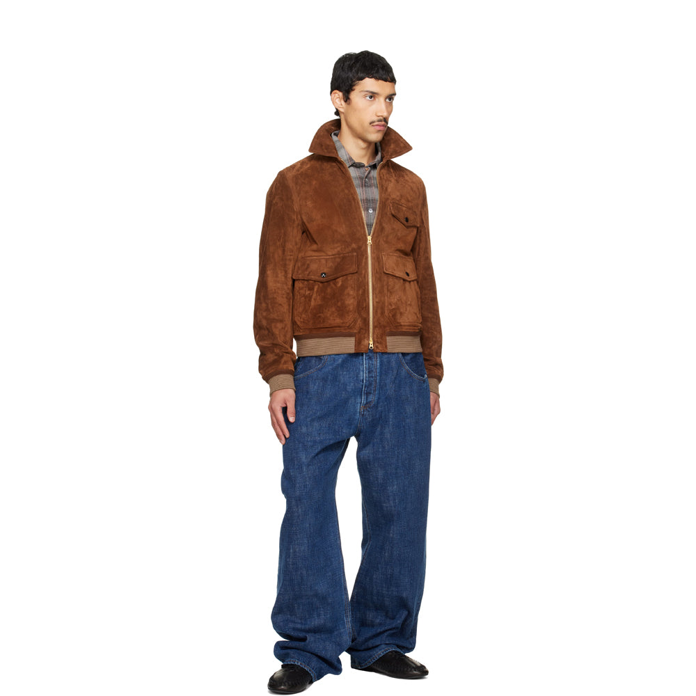 Full-length view of tobacco suede flight bomber worn open with raised collar, wide blue jeans and striped knit trim.